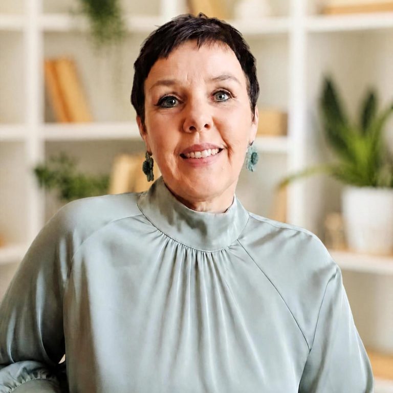 Karen schreibend Frau mit kurzer Frisur, die in ein Notizbuch schreibt, umgeben von Pflanzen und einer Tasse Tee.